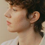 Profile view of a person with curly hair wearing a handcrafted 18k recycled gold earring, showcasing organic design.