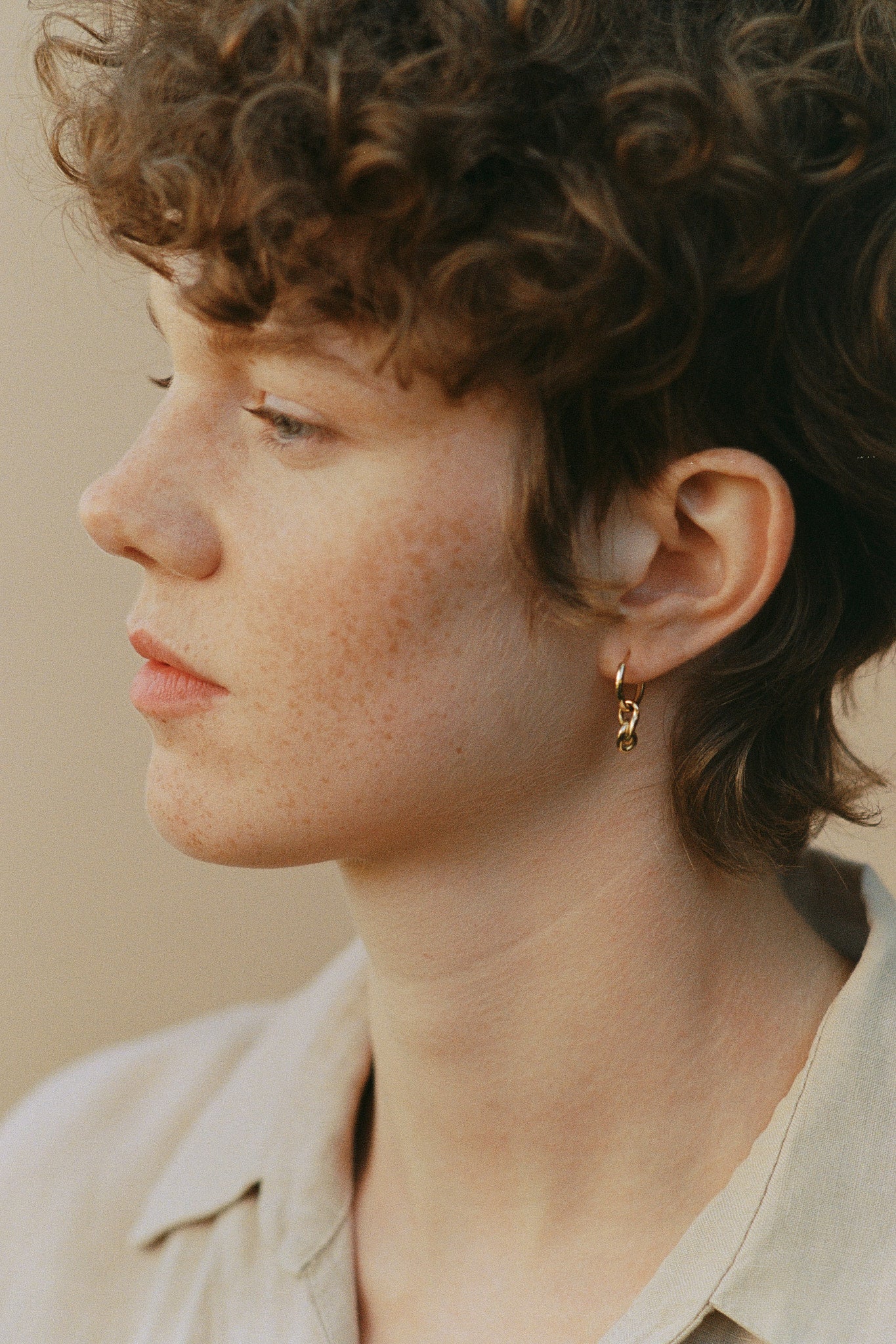 Profile view of a person with curly hair wearing a handcrafted 18k recycled gold earring, showcasing organic design.