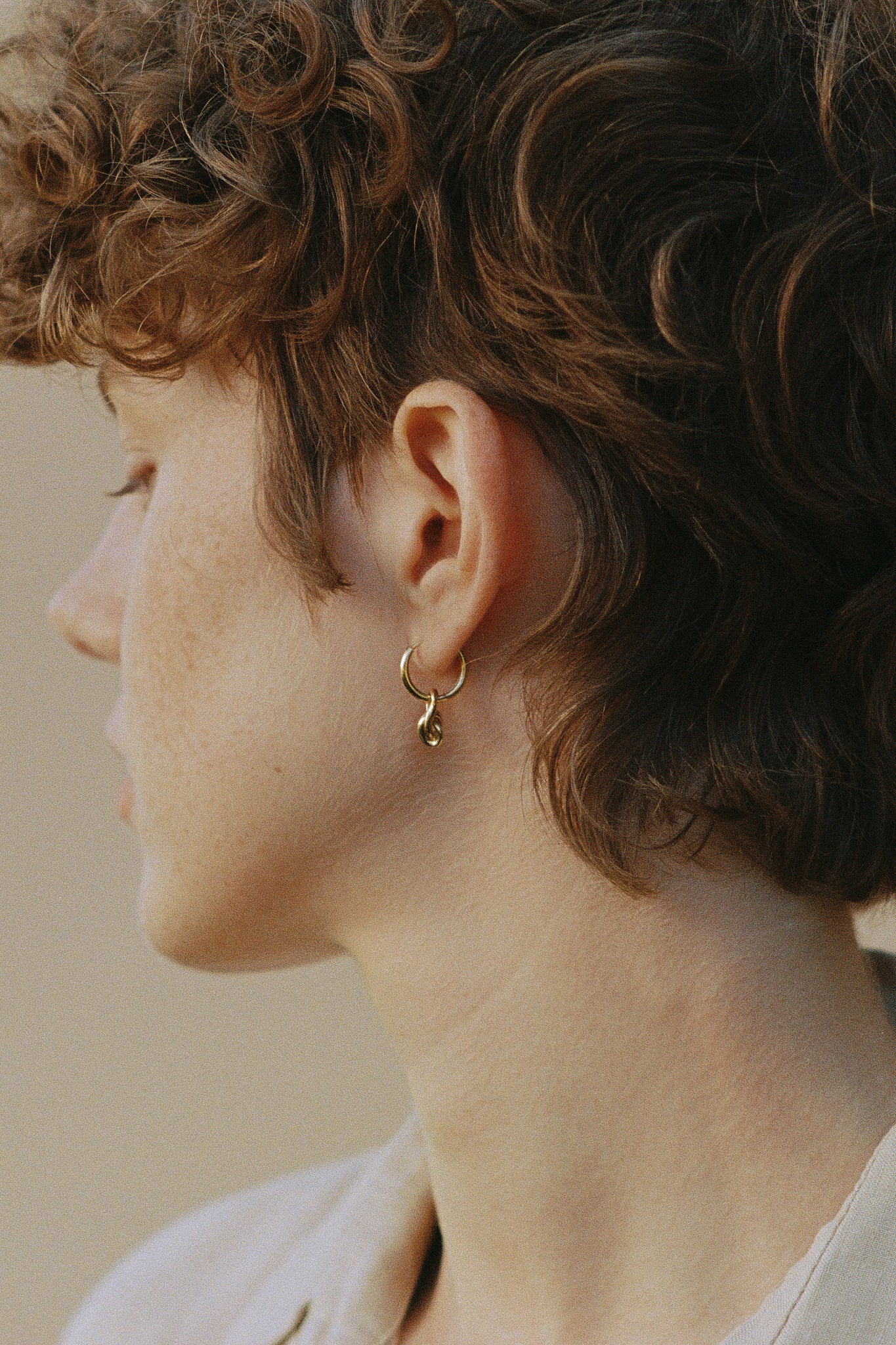 Model wearing SINUOSA hoops in 18k recycled gold, showcasing organic design and craftsmanship from Basel, Switzerland.