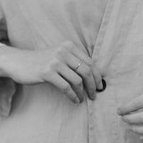 Hand wearing a handcrafted ring, buttoning a light linen garment, showcasing the elegance of 18k recycled gold.