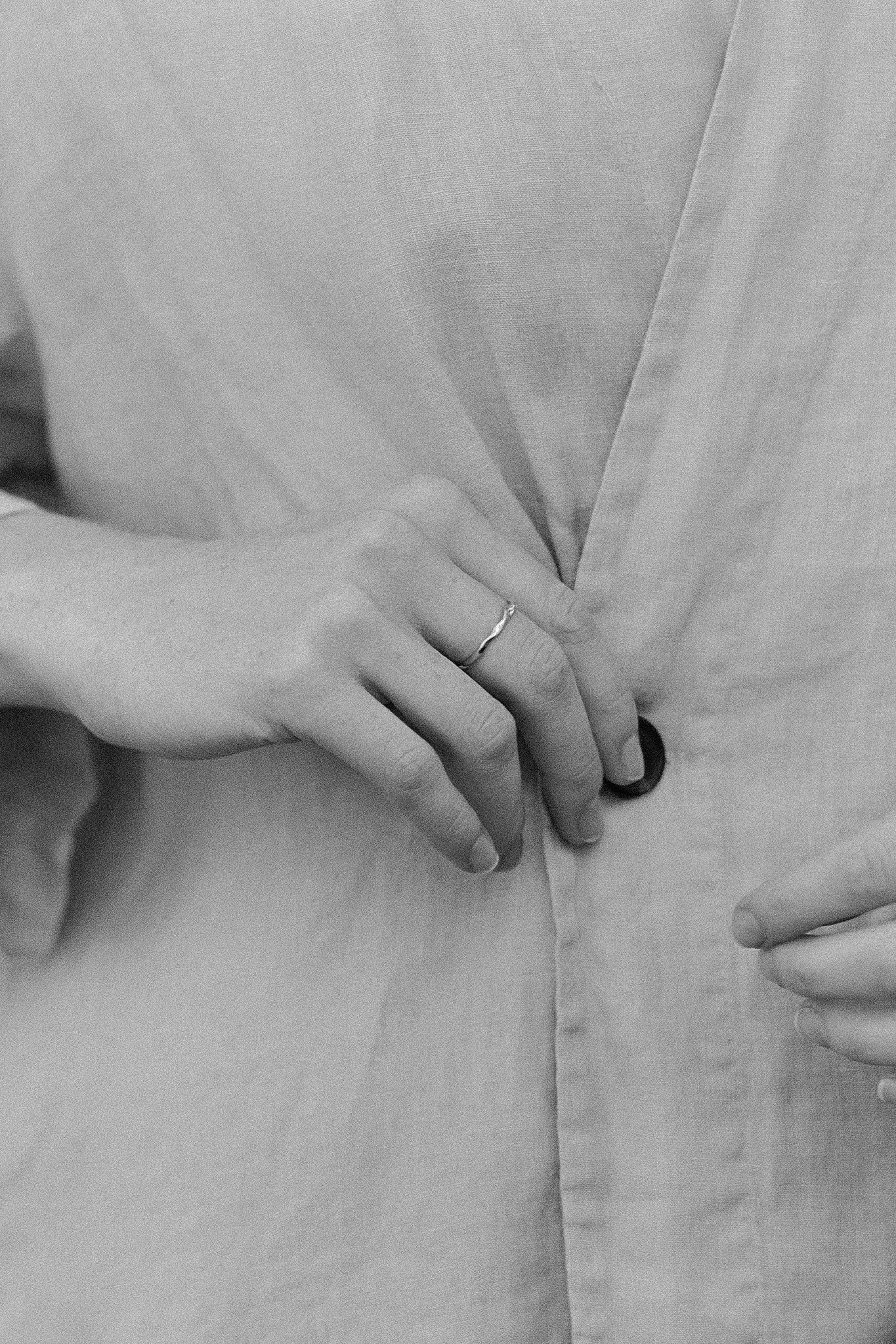Hand wearing a handcrafted ring, buttoning a light linen garment, showcasing the elegance of 18k recycled gold.