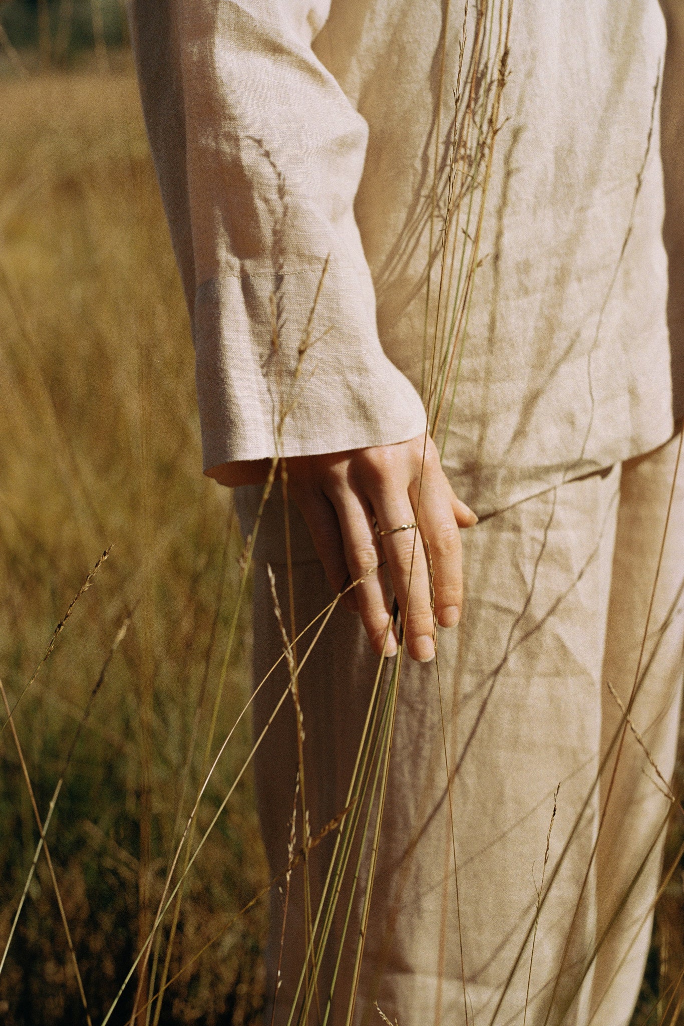 A close-up of a hand holding grass in a field, showcasing natural textures and earthy tones.