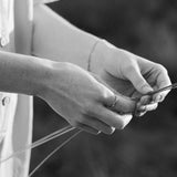 Black and white image of hands delicately working with thin strands of material outdoors.
