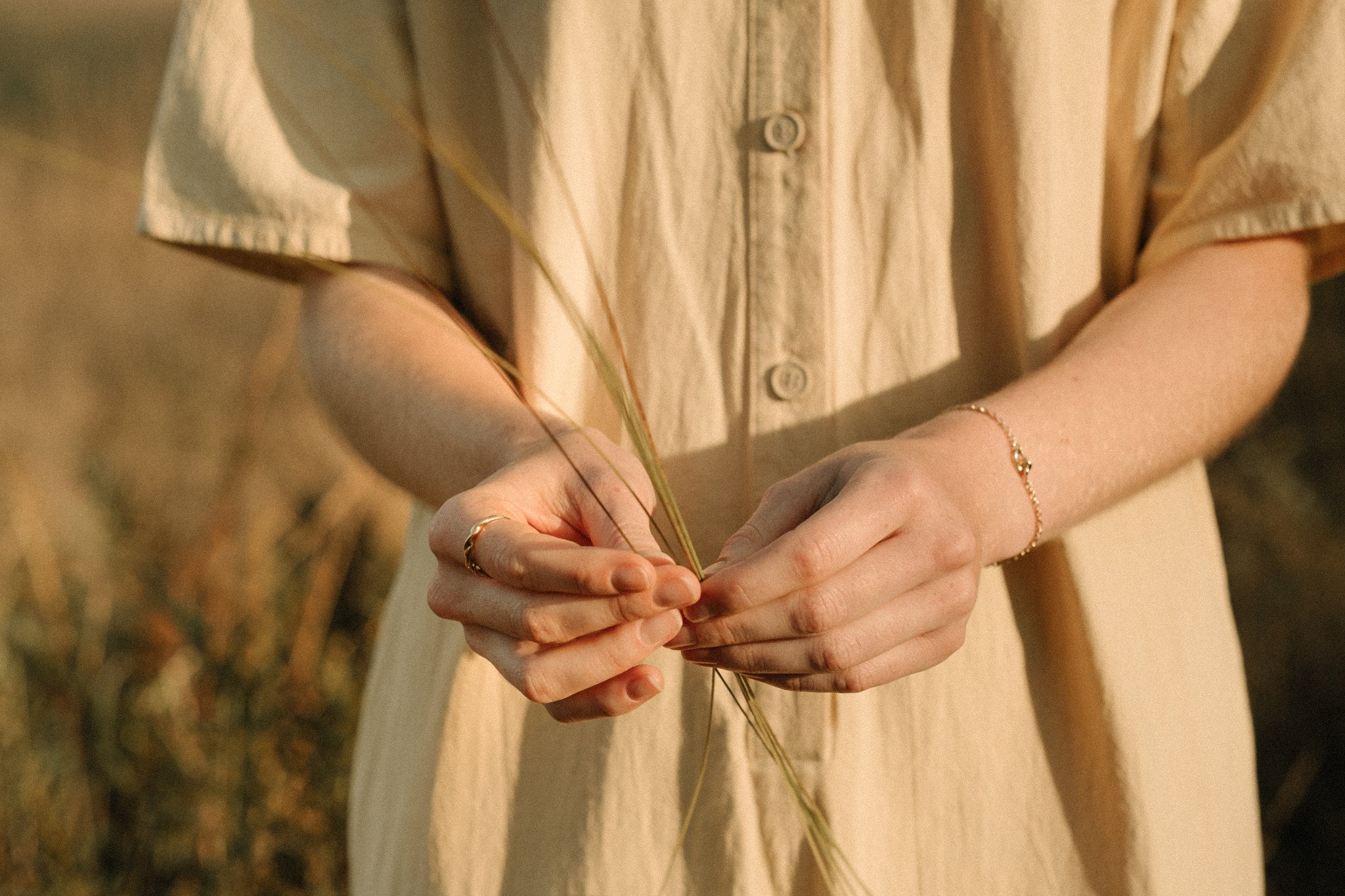 Hands holding grass, wearing a COESA handmade 18k recycled gold bracelet, set against a serene nature backdrop.