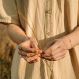 Hands holding grass, wearing a COESA handmade 18k recycled gold bracelet, set against a serene nature backdrop.