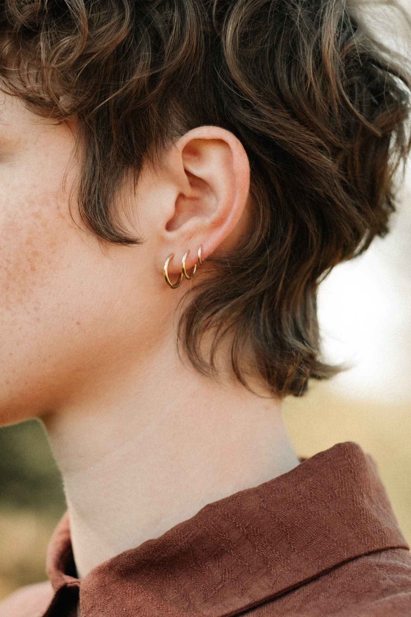 Profile view of a person wearing 18k recycled gold LOA hoops, showcasing their handcrafted design from Basel, Switzerland.