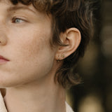 Close-up of a person wearing handcrafted TOVE small studs in 18k recycled gold, highlighting a shiny surface.