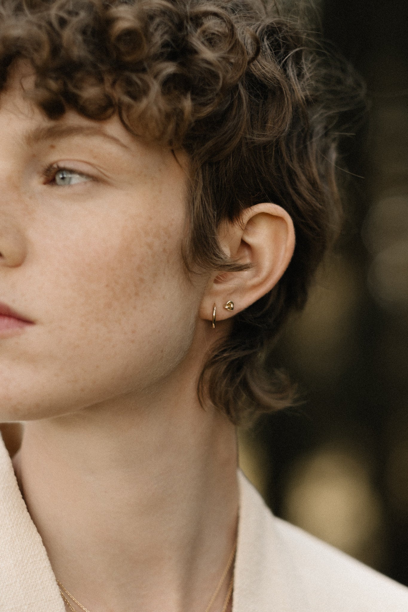 Close-up of a person wearing handcrafted TOVE small studs in 18k recycled gold, highlighting a shiny surface.