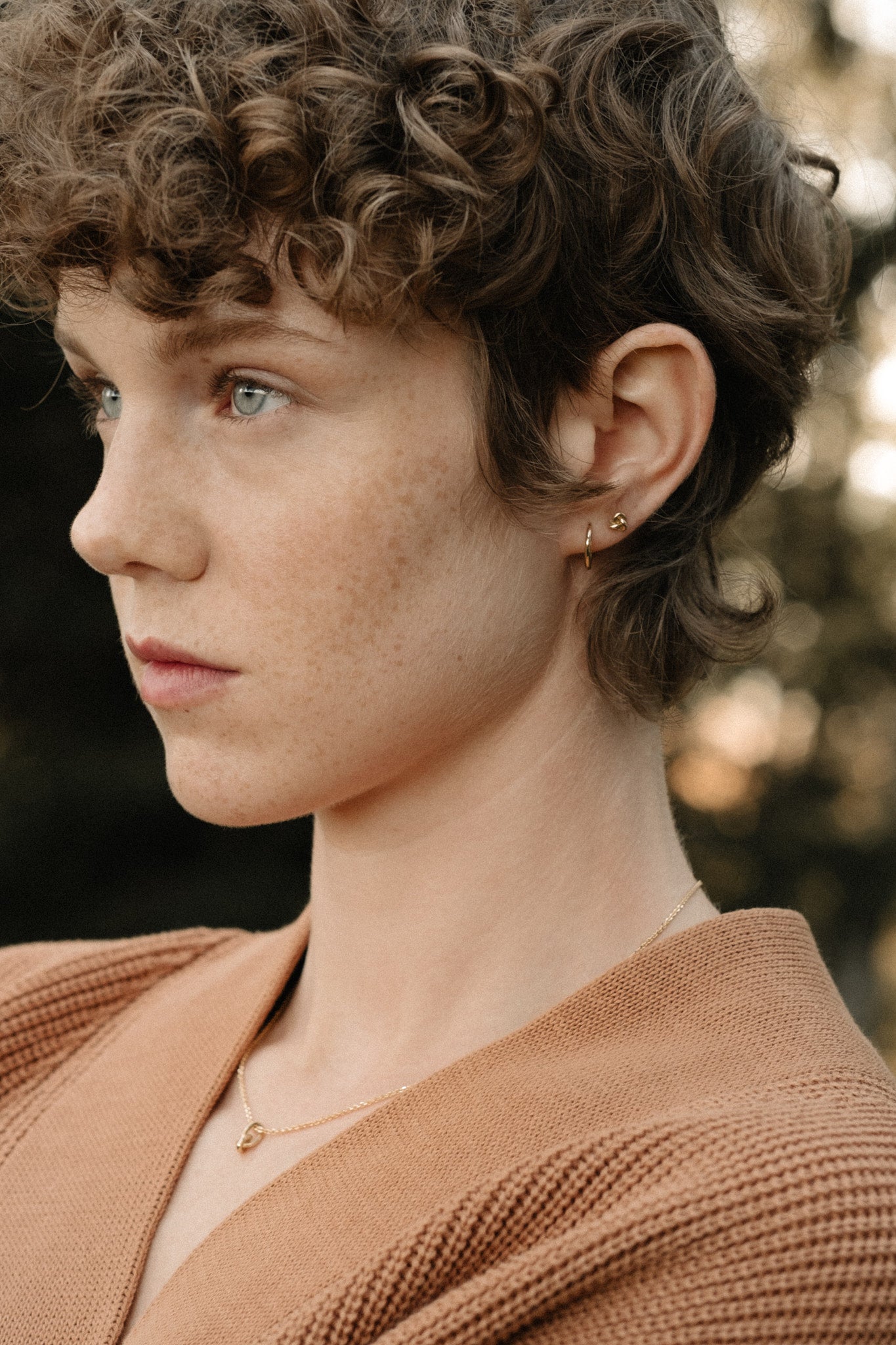 Side profile of a person with curly hair wearing handcrafted 18k recycled gold jewelry.