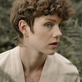 A model wearing a TOVE necklace made of 18k recycled gold, surrounded by lush ferns, showcasing sustainable handcrafted jewelry.