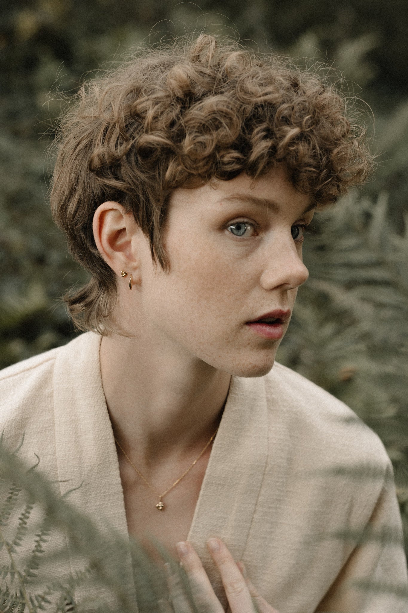 A model wearing a TOVE necklace made of 18k recycled gold, surrounded by lush ferns, showcasing sustainable handcrafted jewelry.