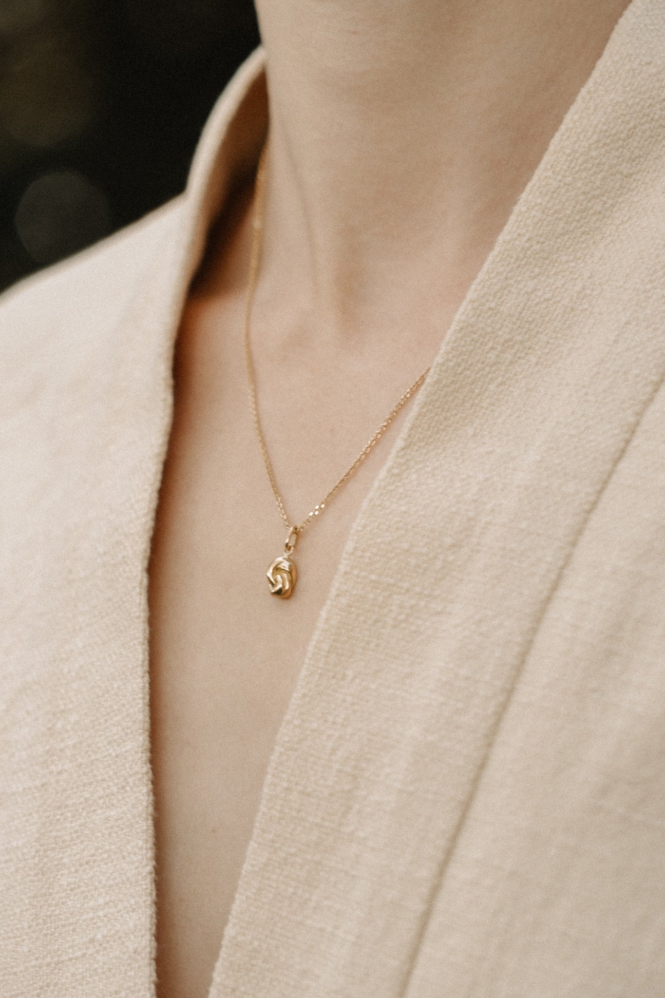 Handcrafted 18k recycled gold TWINE necklace worn on a beige garment, designed in Basel, Switzerland.