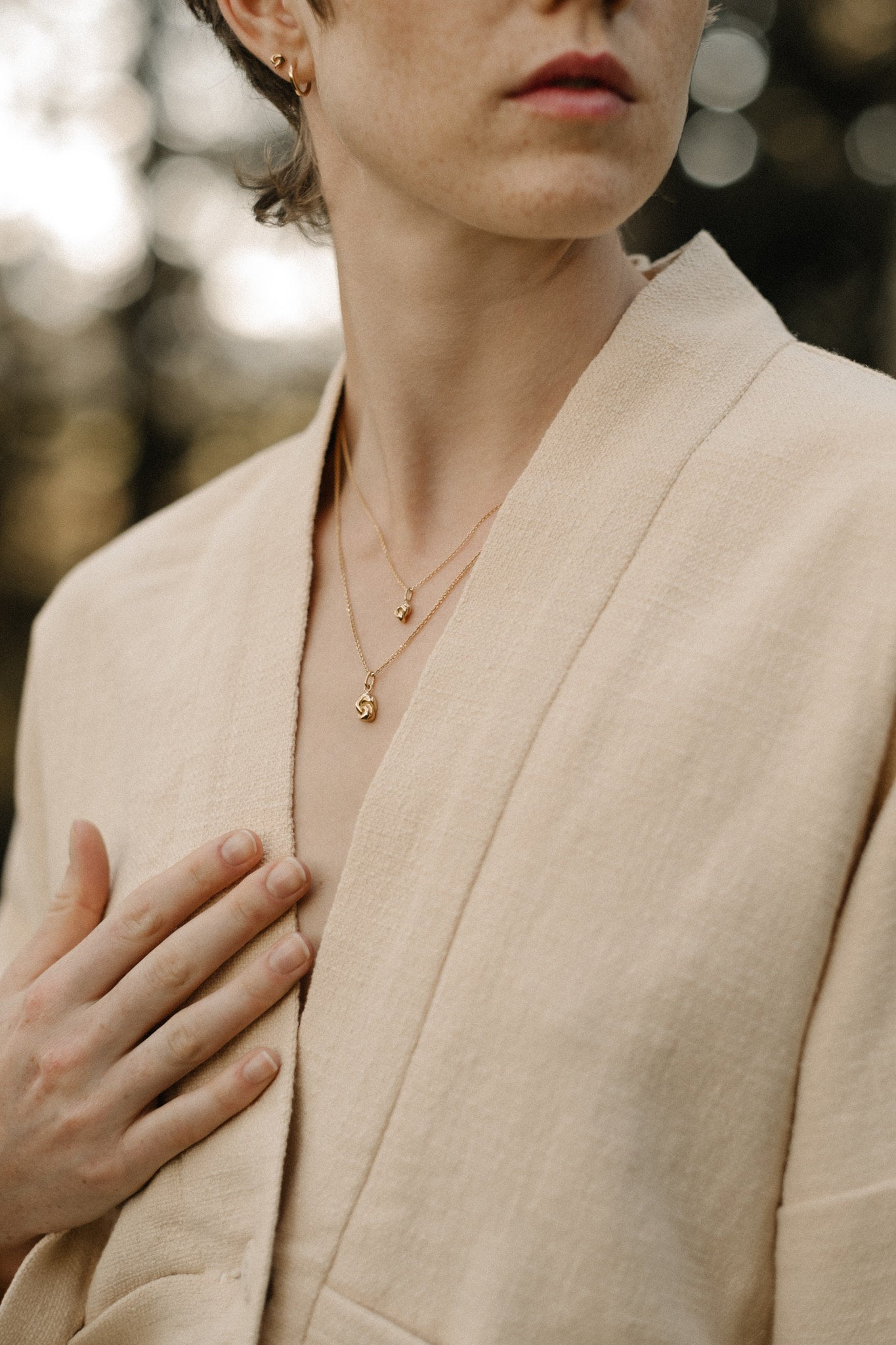 Close-up of a model wearing a beige jacket with layered necklaces featuring organic designs handcrafted in Basel, Switzerland.
