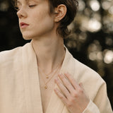 Model wearing TOVE 18k recycled gold necklace in a natural outdoor setting, showcasing sustainable, handcrafted elegance.