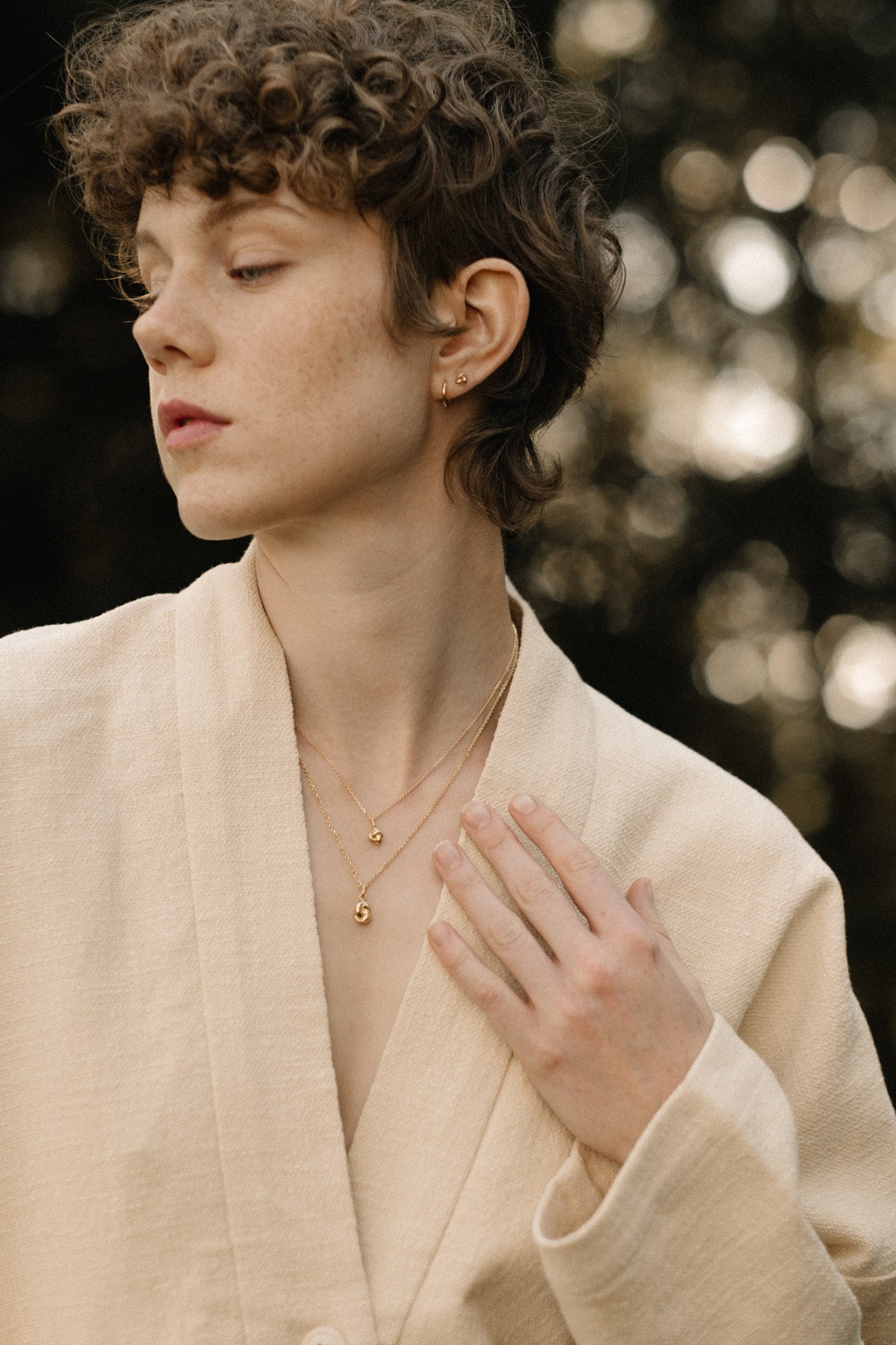 Model wearing TOVE 18k recycled gold necklace in a natural outdoor setting, showcasing sustainable, handcrafted elegance.
