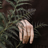 Hand wearing a handcrafted 18k recycled gold ring, gently holding a fern in a natural setting.