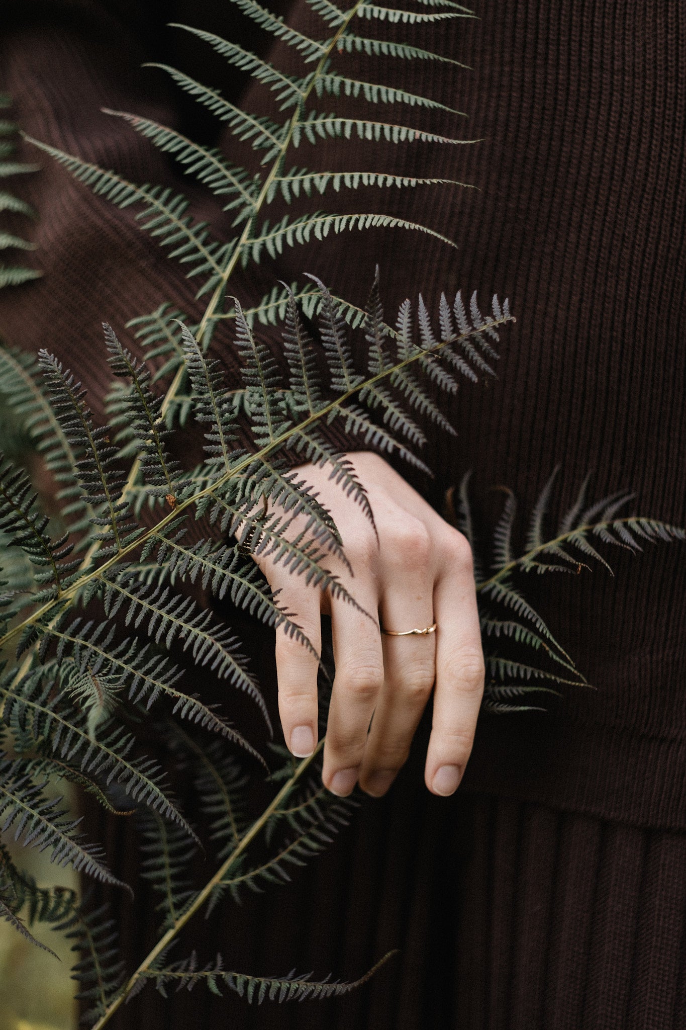 Hand wearing a handcrafted 18k recycled gold ring, gently holding a fern in a natural setting.