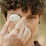 Model holding a sea shell while wearing a handcrafted TWINE ring made of 18k recycled gold.