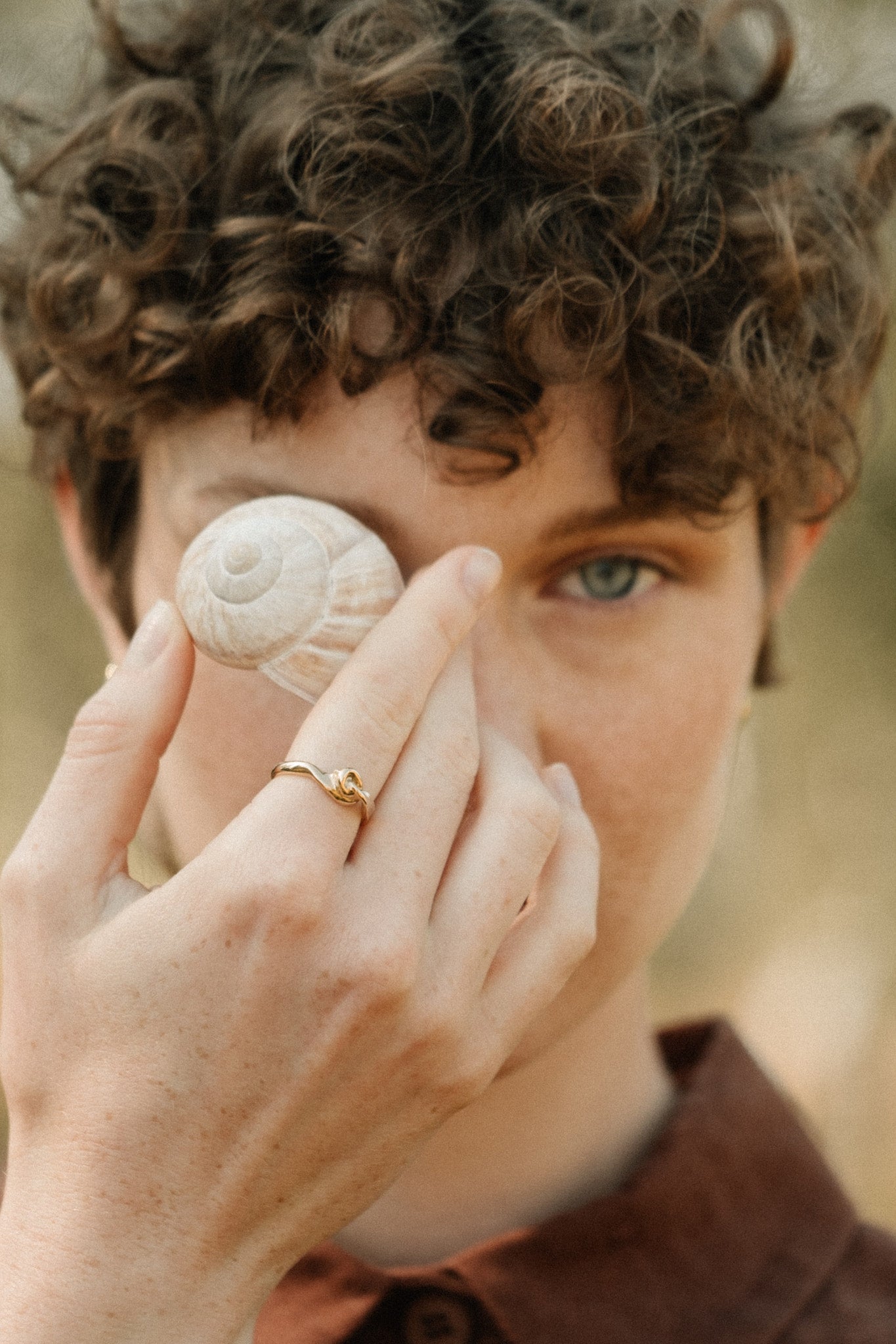 Model holding a sea shell while wearing a handcrafted TWINE ring made of 18k recycled gold.