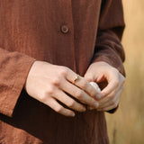 Handcrafted TWINE ring in 18k recycled gold worn by a person in a brown outfit in a natural setting.