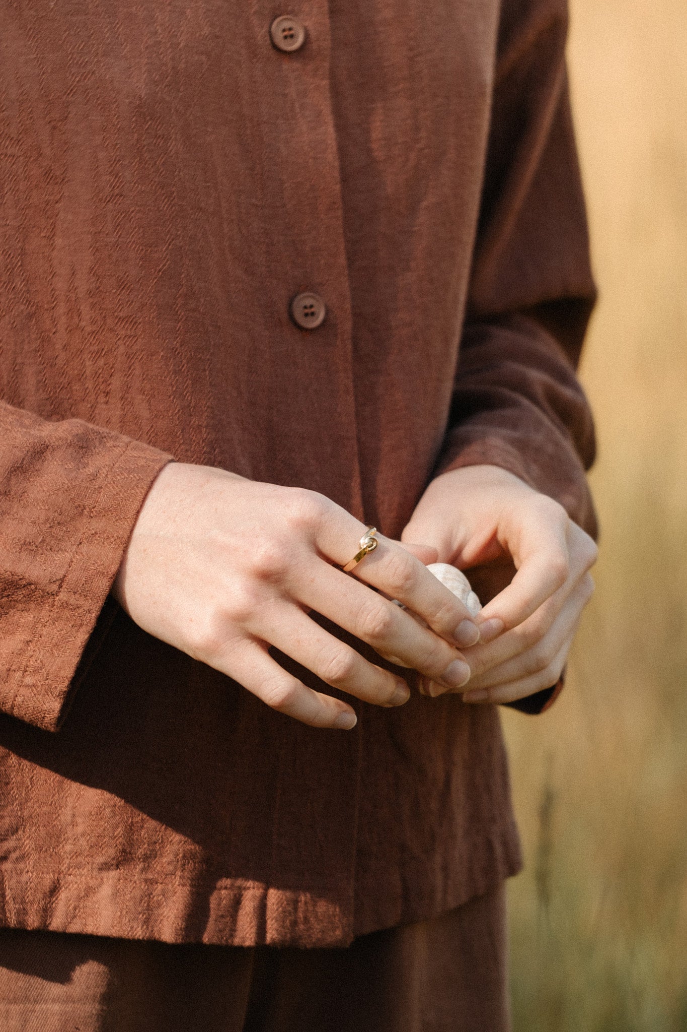 Handcrafted TWINE ring in 18k recycled gold worn by a person in a brown outfit in a natural setting.