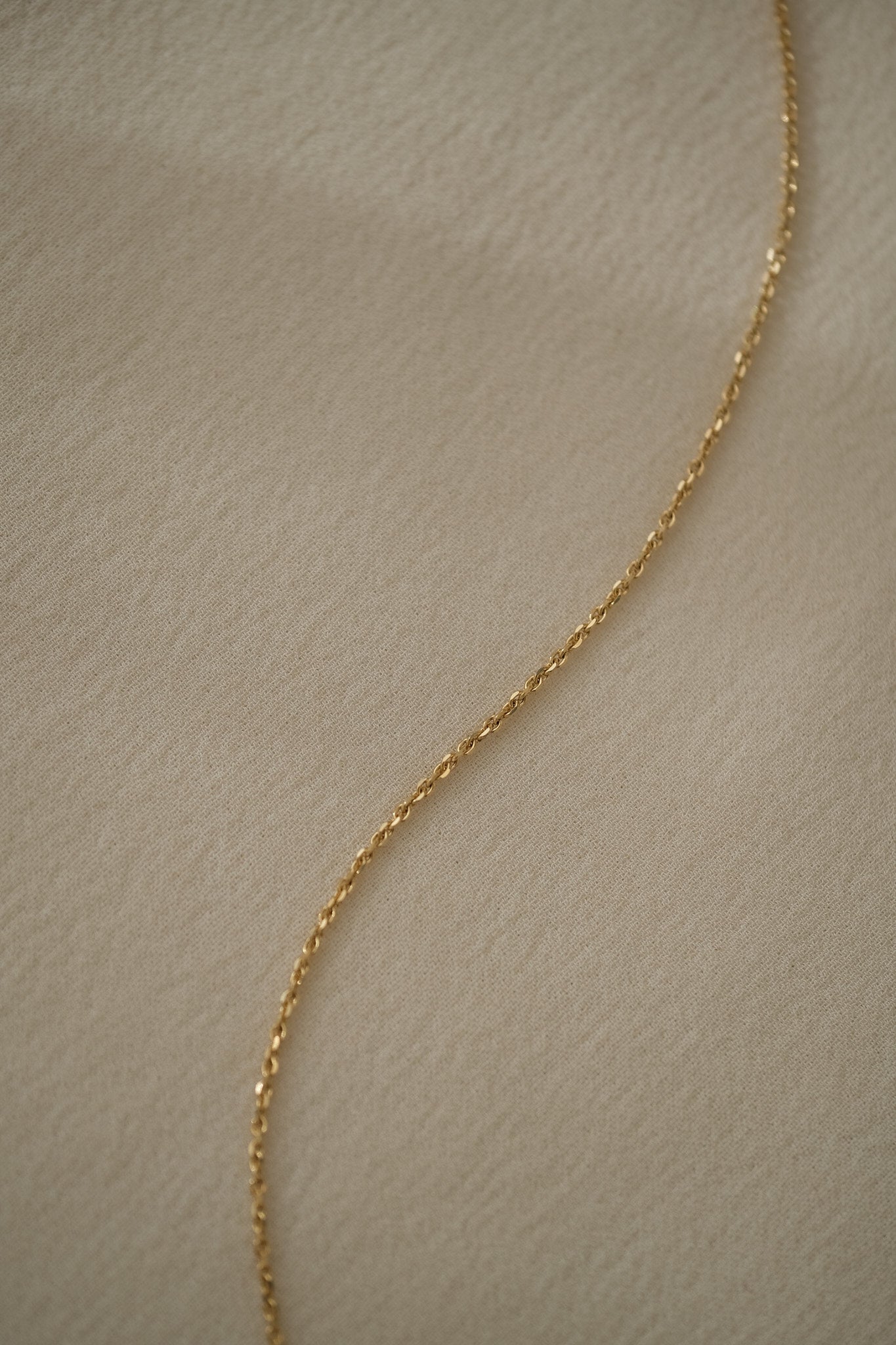 Elegant 18k recycled gold chain on soft fabric, handcrafted in Basel, Switzerland, showcasing organic design and craftsmanship.