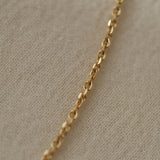 Close-up of a handcrafted 18k recycled gold chain, showcasing its organic faceted links on a soft fabric background.