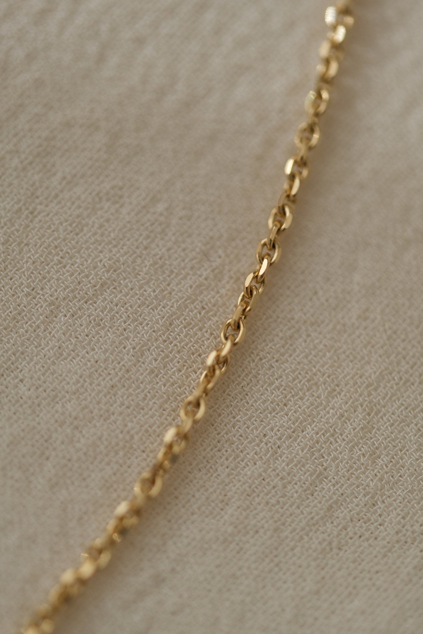 Close-up of a handcrafted 18k recycled gold chain, showcasing its organic faceted links on a soft fabric background.