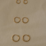 Three sets of handcrafted 18k recycled gold hoops in various sizes on a soft textured background.