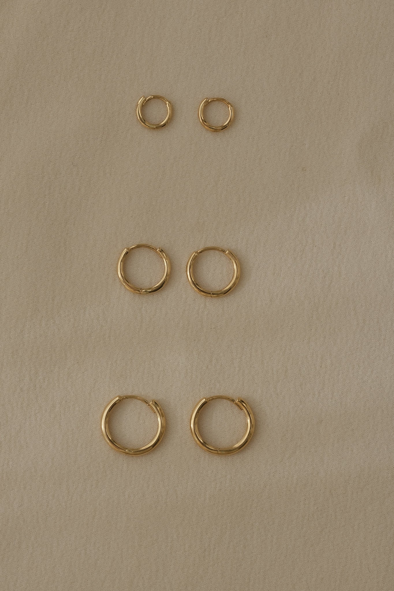 Three sets of handcrafted 18k recycled gold hoops in various sizes on a soft textured background.