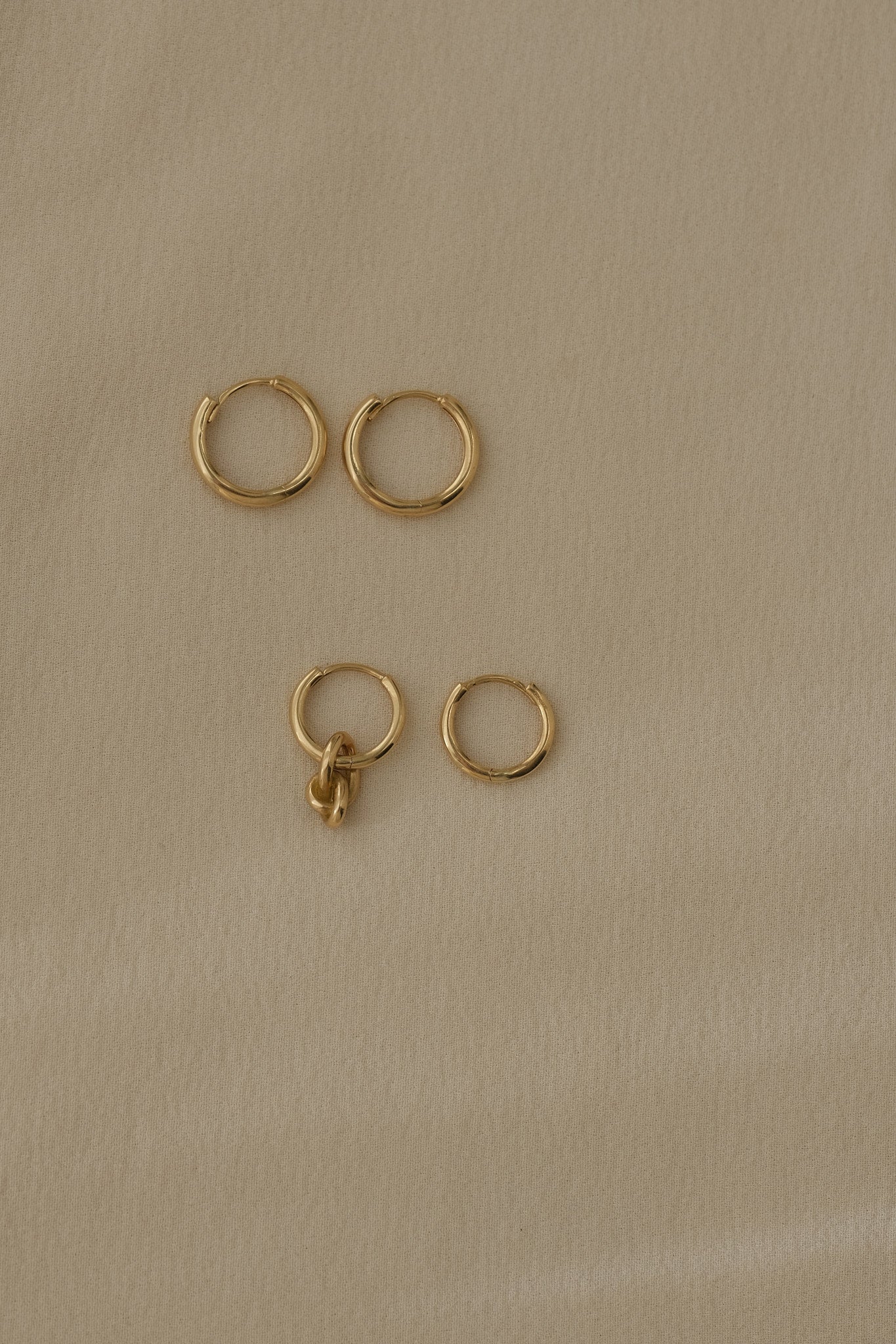 Handcrafted 18k recycled gold hoops in various sizes on soft beige background, made in Basel, Switzerland.