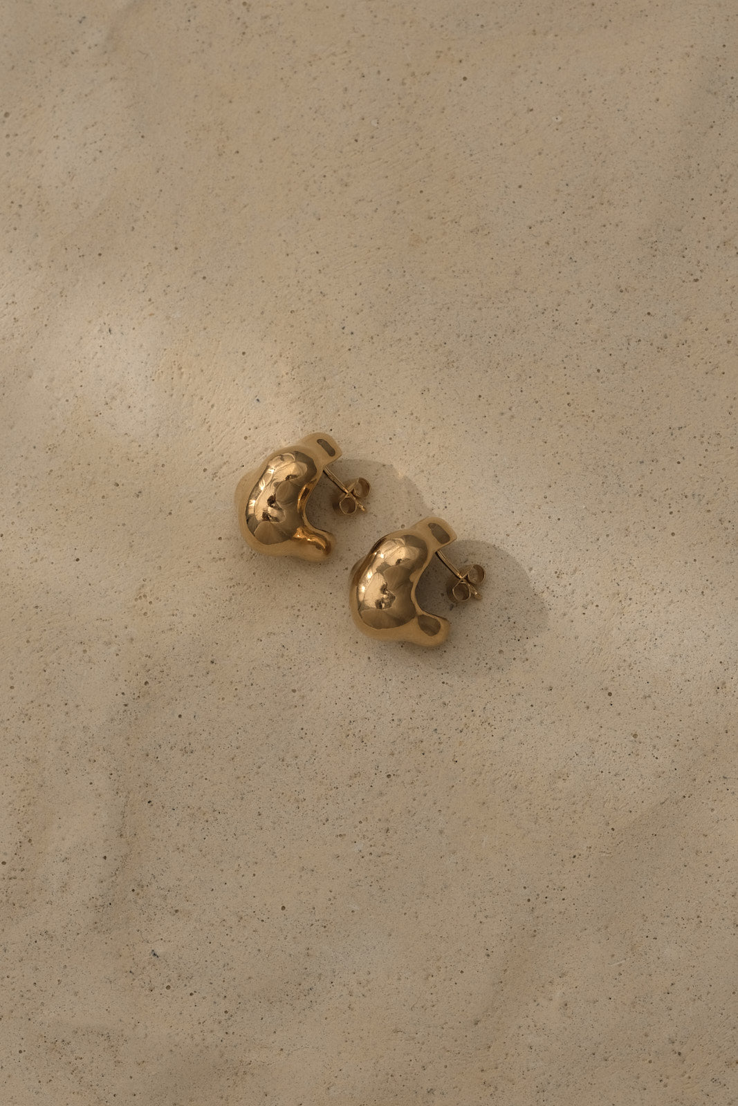 CLOUD earrings in recycled gold, ethically handcrafted, showcasing sustainable jewelry design on sandy surface.