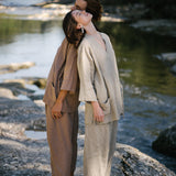 Two models in natural fabrics pose back-to-back by a river, showcasing sustainable fashion styles.