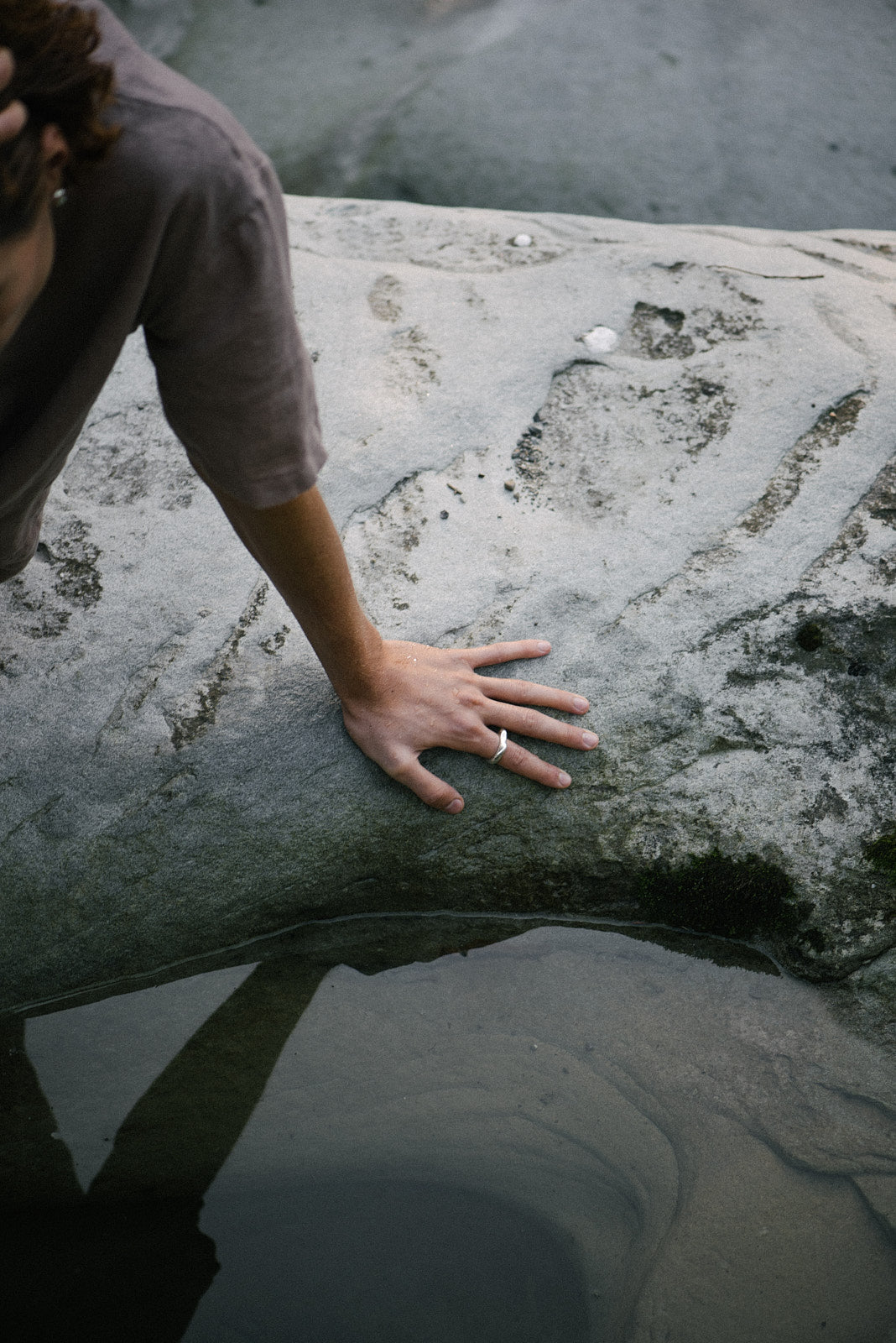 Hand resting on a rock near water, showcasing the DUNA ring made of recycled gold and silver. Ethical jewelry in nature.