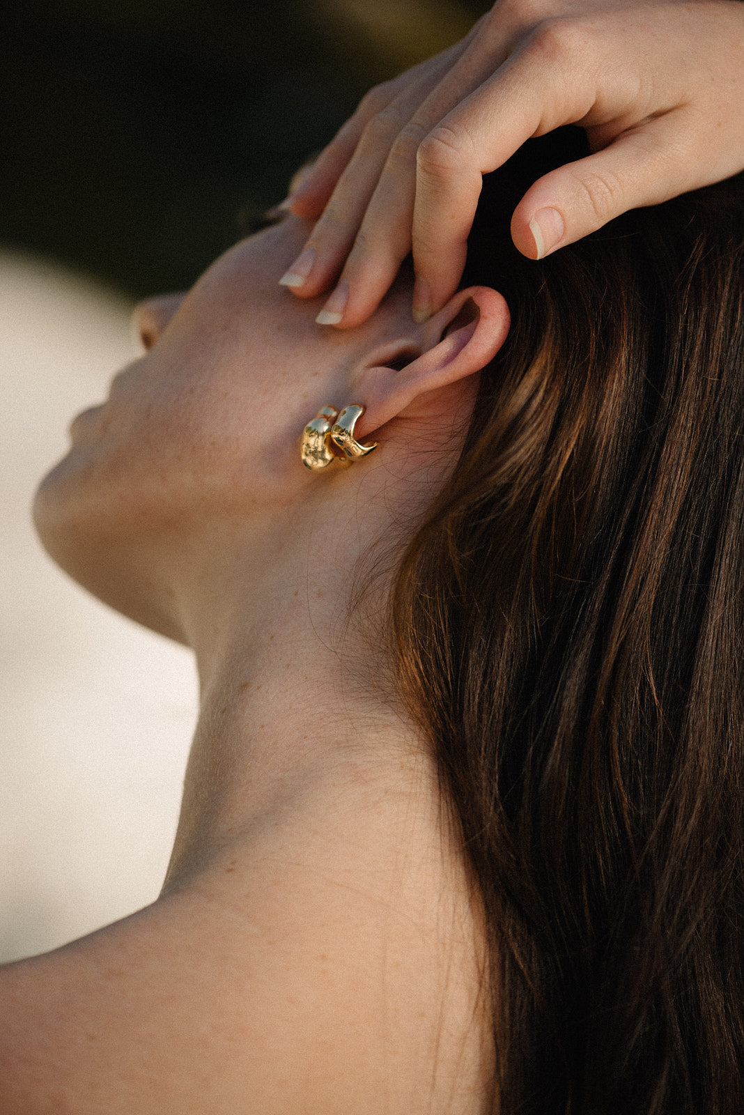 Elegant woman wearing FLUID earrings, handmade from sustainable materials in recycled gold and silver.