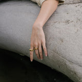 Hand wearing FLUID ring made of recycled gold and silver, showcasing ethical handmade jewelry in a natural setting.