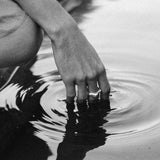 A hand gently touching the surface of water, creating ripples, in black and white.