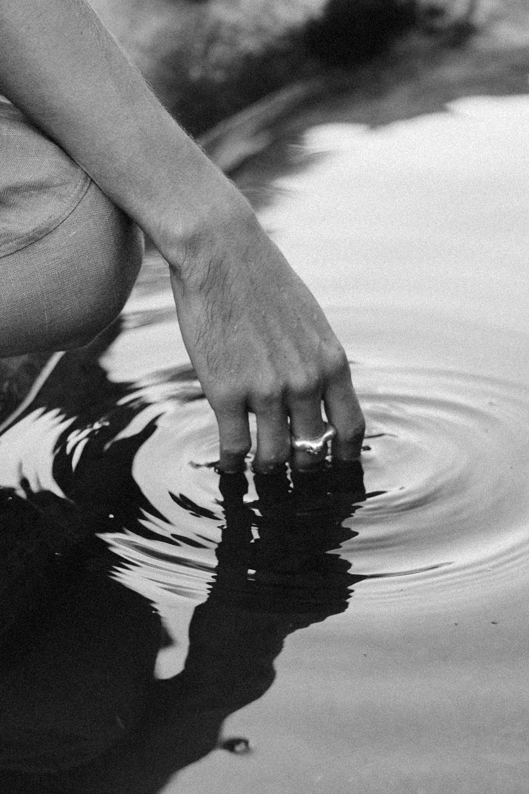 A hand gently touching the surface of water, creating ripples, in black and white.