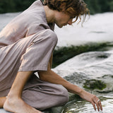 Person in natural setting touching water, wearing sustainable fashion, embodying a connection to nature.