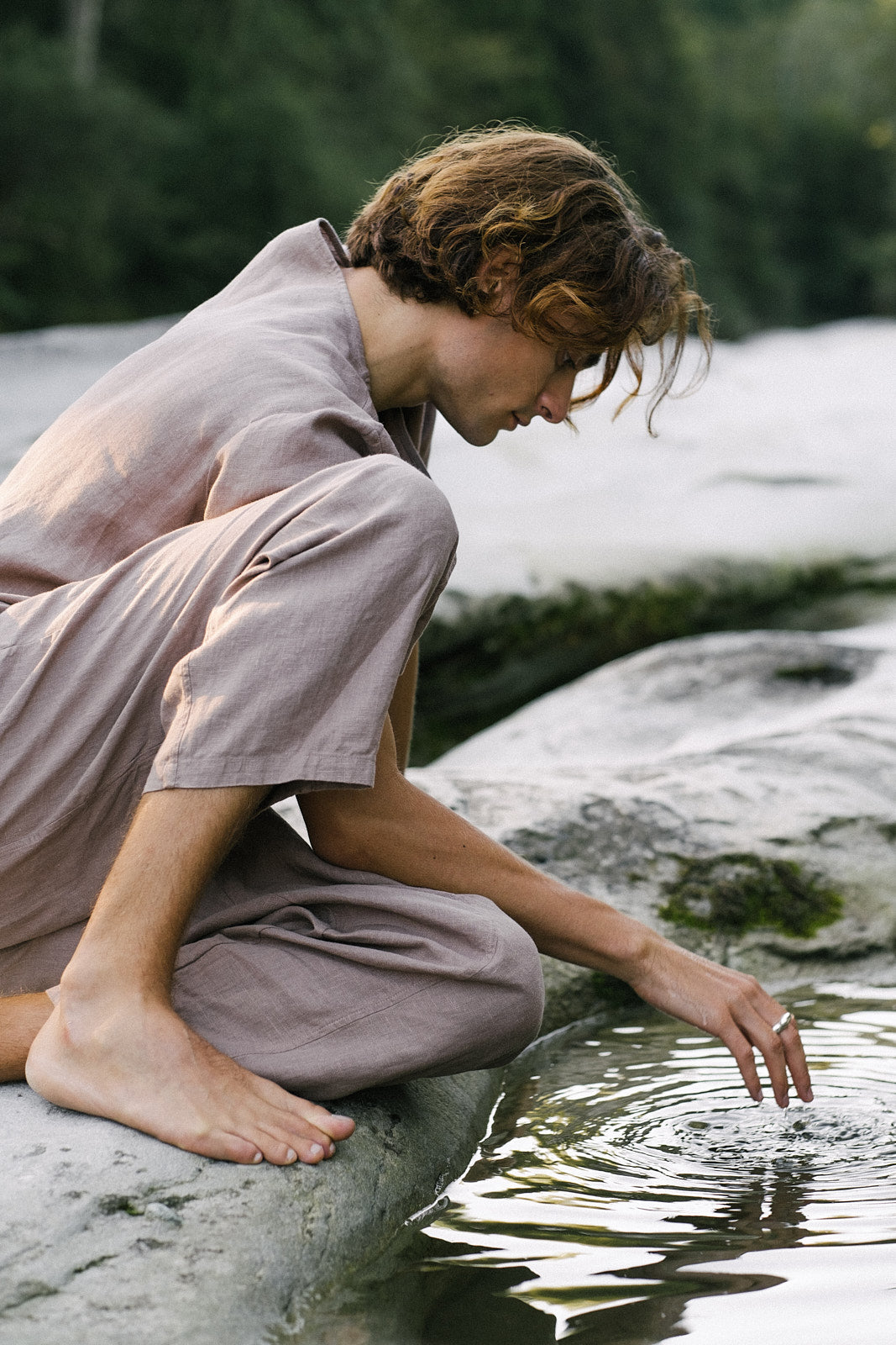 Person in natural setting touching water, wearing sustainable fashion, embodying a connection to nature.