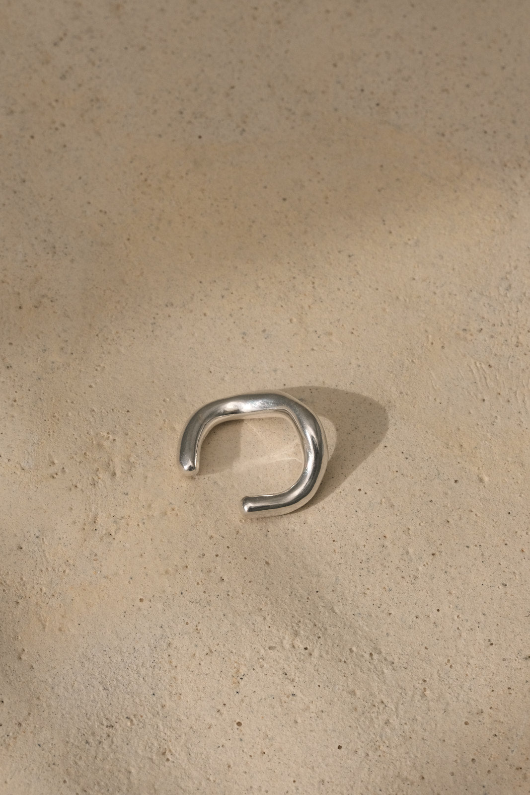 MISMO earcuff in recycled silver on textured surface, highlighting sustainable handmade ethical jewelry.