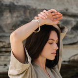 Woman wearing MUSA bangle made from recycled gold, showcasing ethical jewelry in a natural setting.