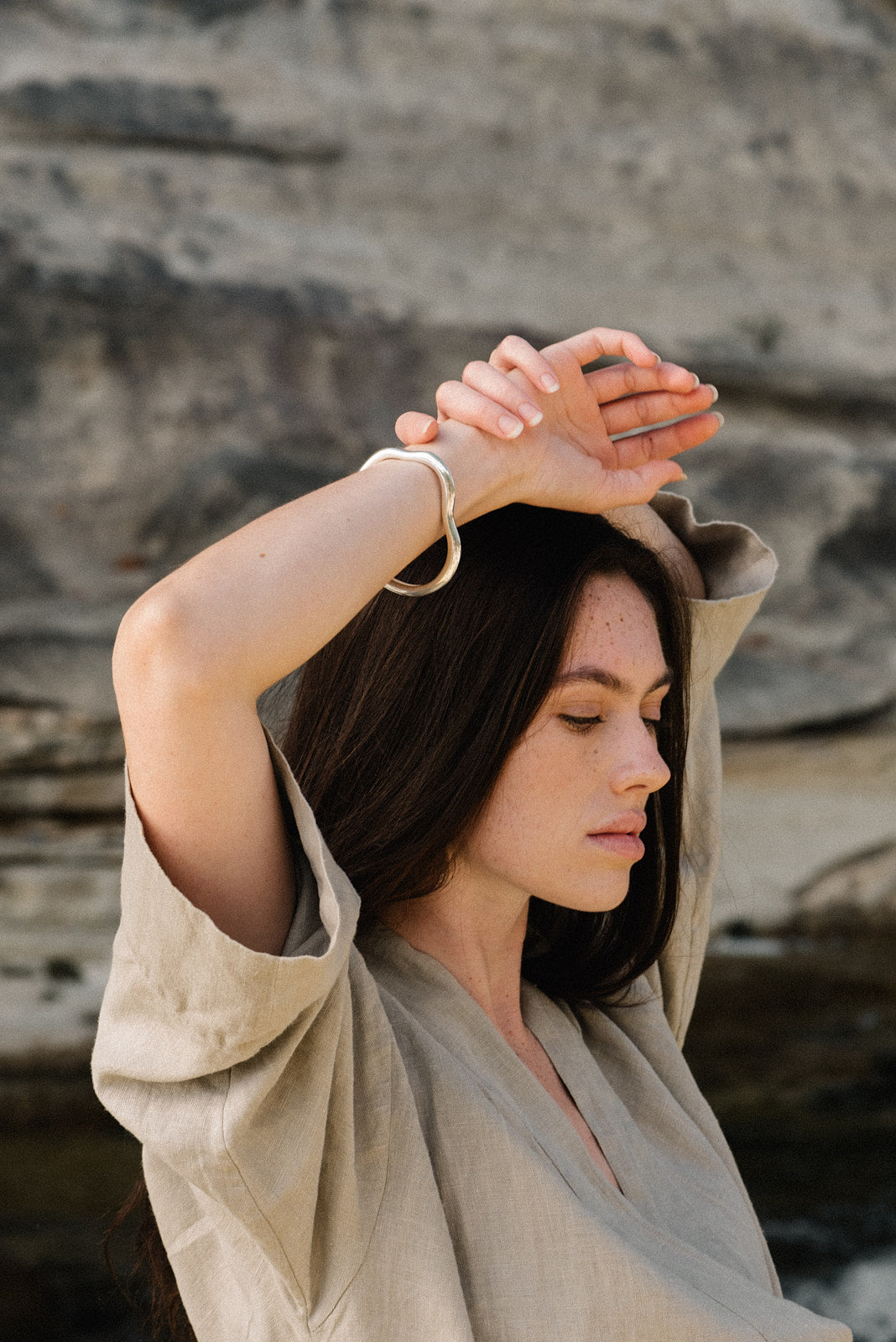 Woman wearing MUSA bangle made from recycled gold, showcasing ethical jewelry in a natural setting.