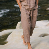 Model wearing a sustainable, handmade linen outfit standing barefoot on a rock by a river.
