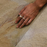 Hand wearing MUSA ring made of recycled silver, showcasing ethical jewelry on natural stone surface.