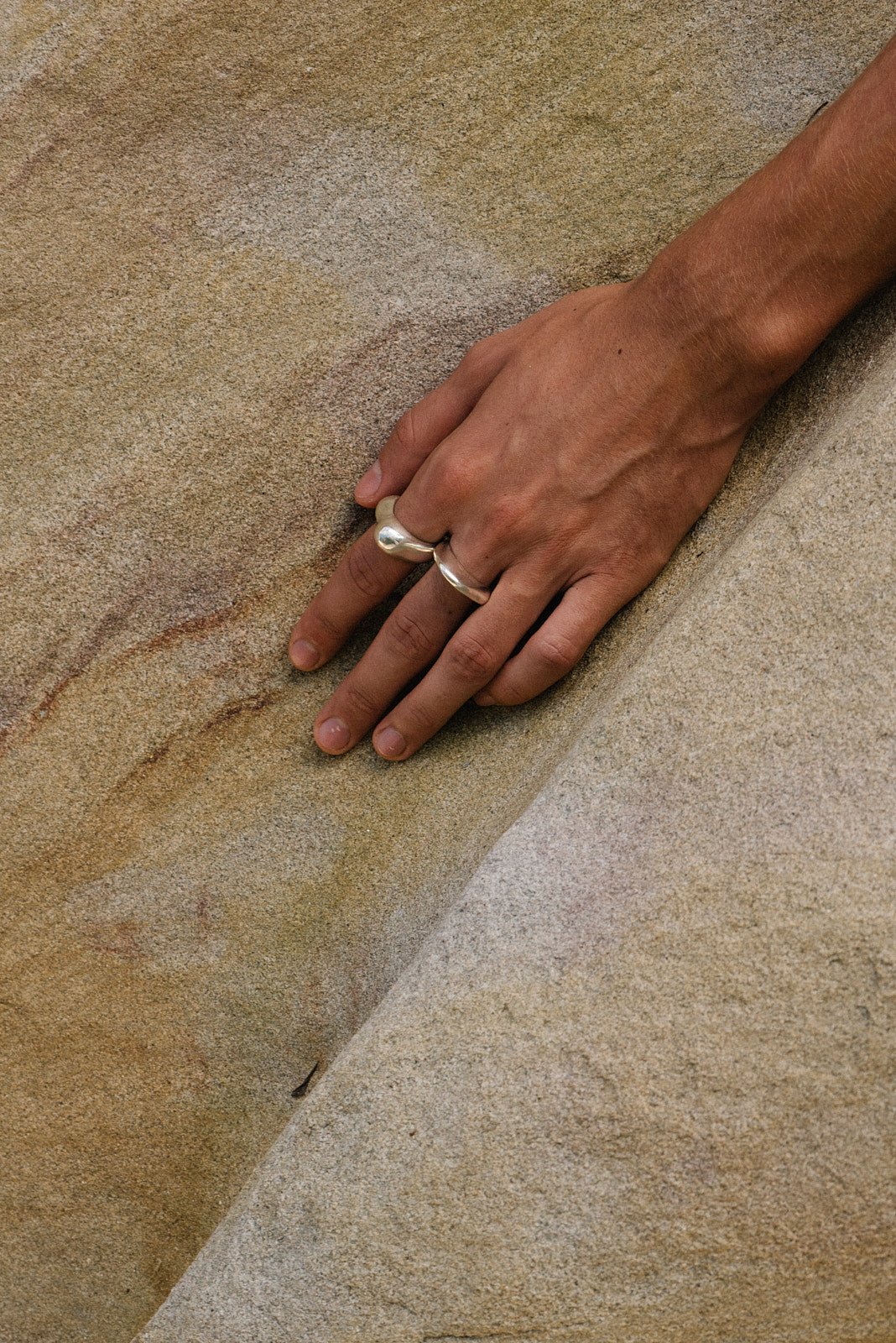 Hand wearing MUSA ring made of recycled silver, showcasing ethical jewelry on natural stone surface.