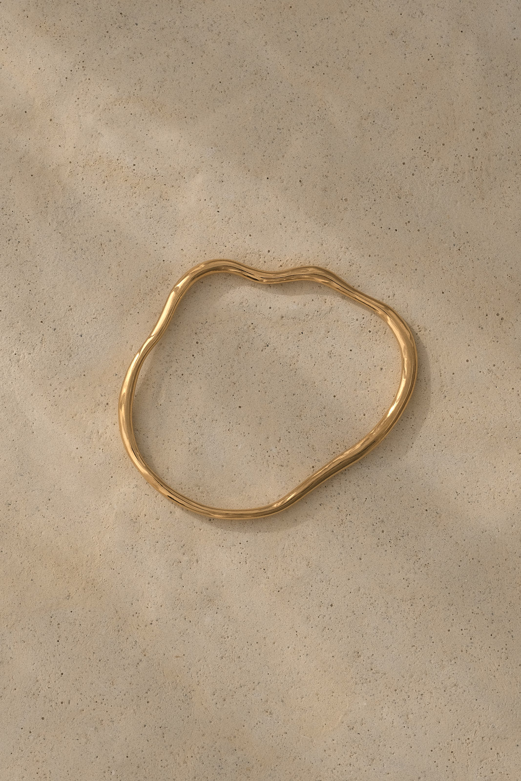 Handmade ethical jewelry PLACID bangle in 18k gold-plated recycled silver on a textured surface.