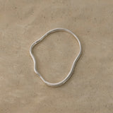 Handmade PLACID bangle in recycled silver on a beige background, showcasing ethical jewelry craftsmanship.