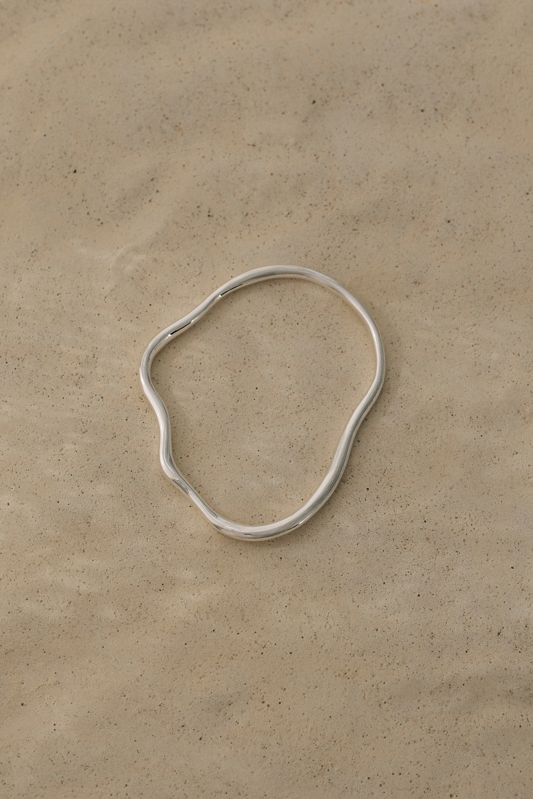 Handmade PLACID bangle in recycled silver on a beige background, showcasing ethical jewelry craftsmanship.