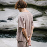 Model wearing sustainable beige outfit standing near water, showcasing an ethical lifestyle in nature.